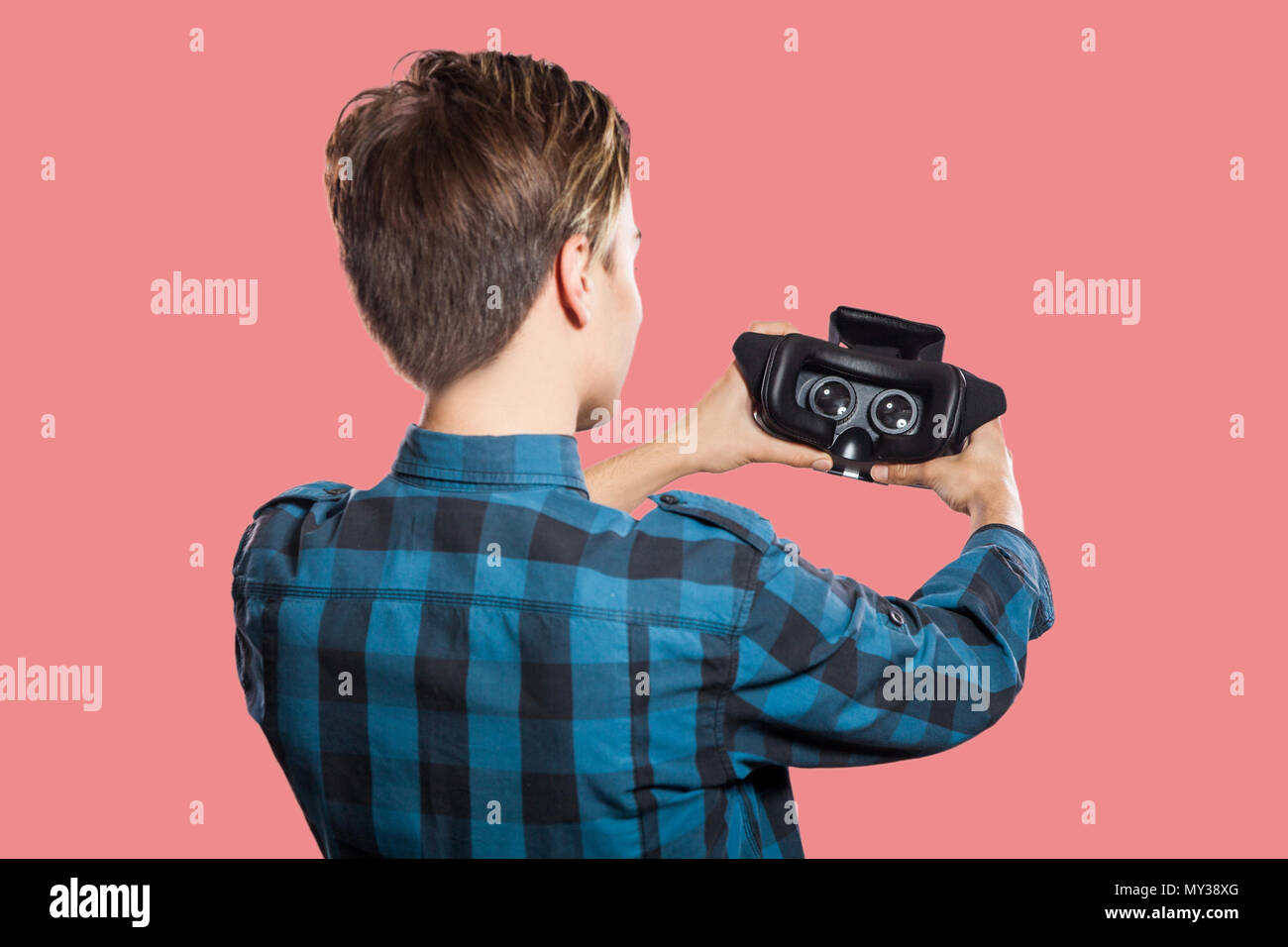 back view of young man holding vr headset. studio shot, isolated on pink background. Stock Photo