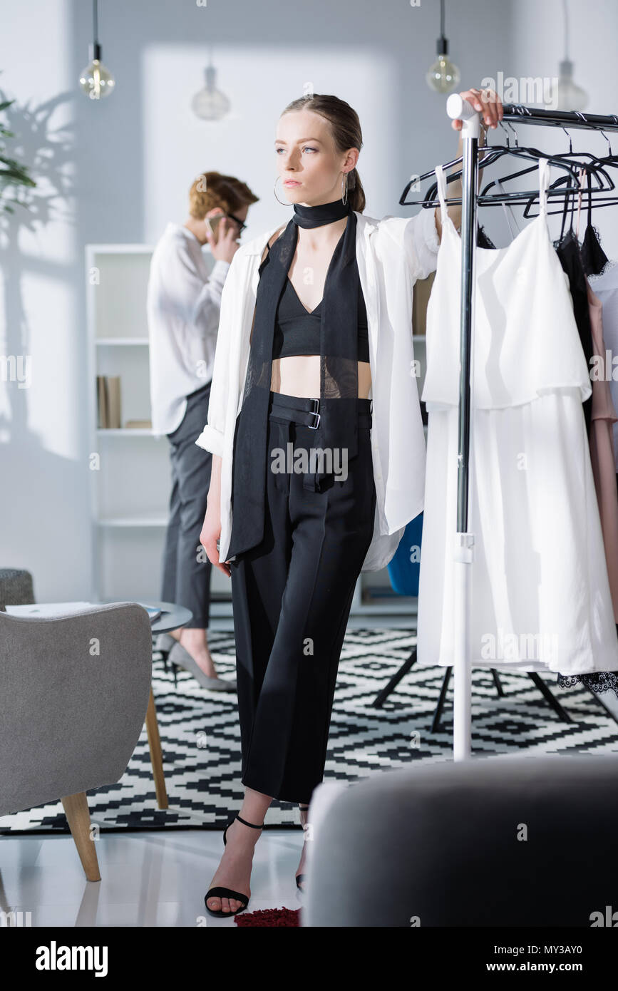young fashion designer leaning on rack at office while colleague ...
