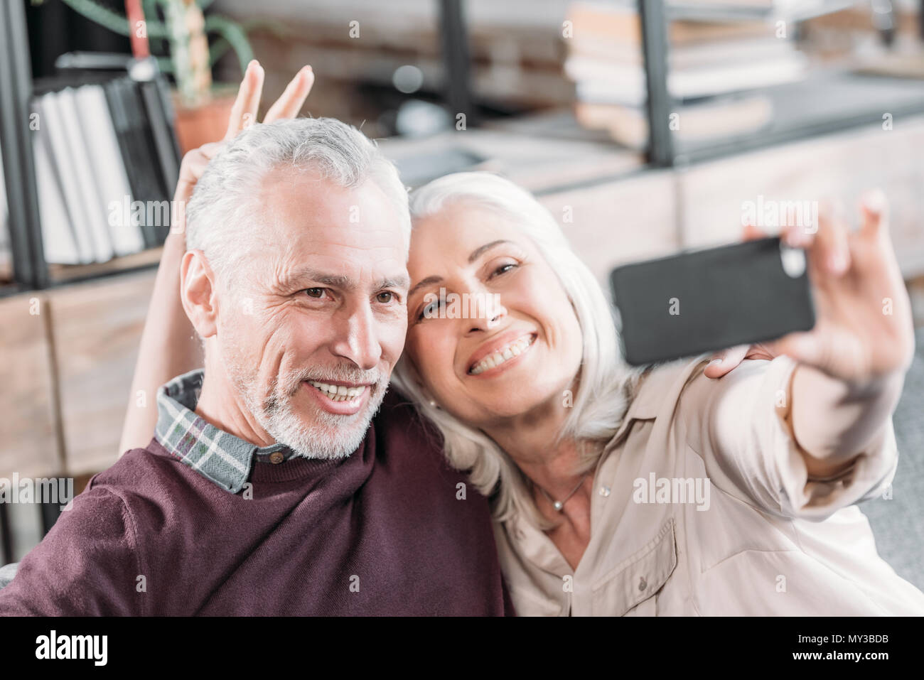 Happy senior couple having fun while taking selfie on sofa at home ...