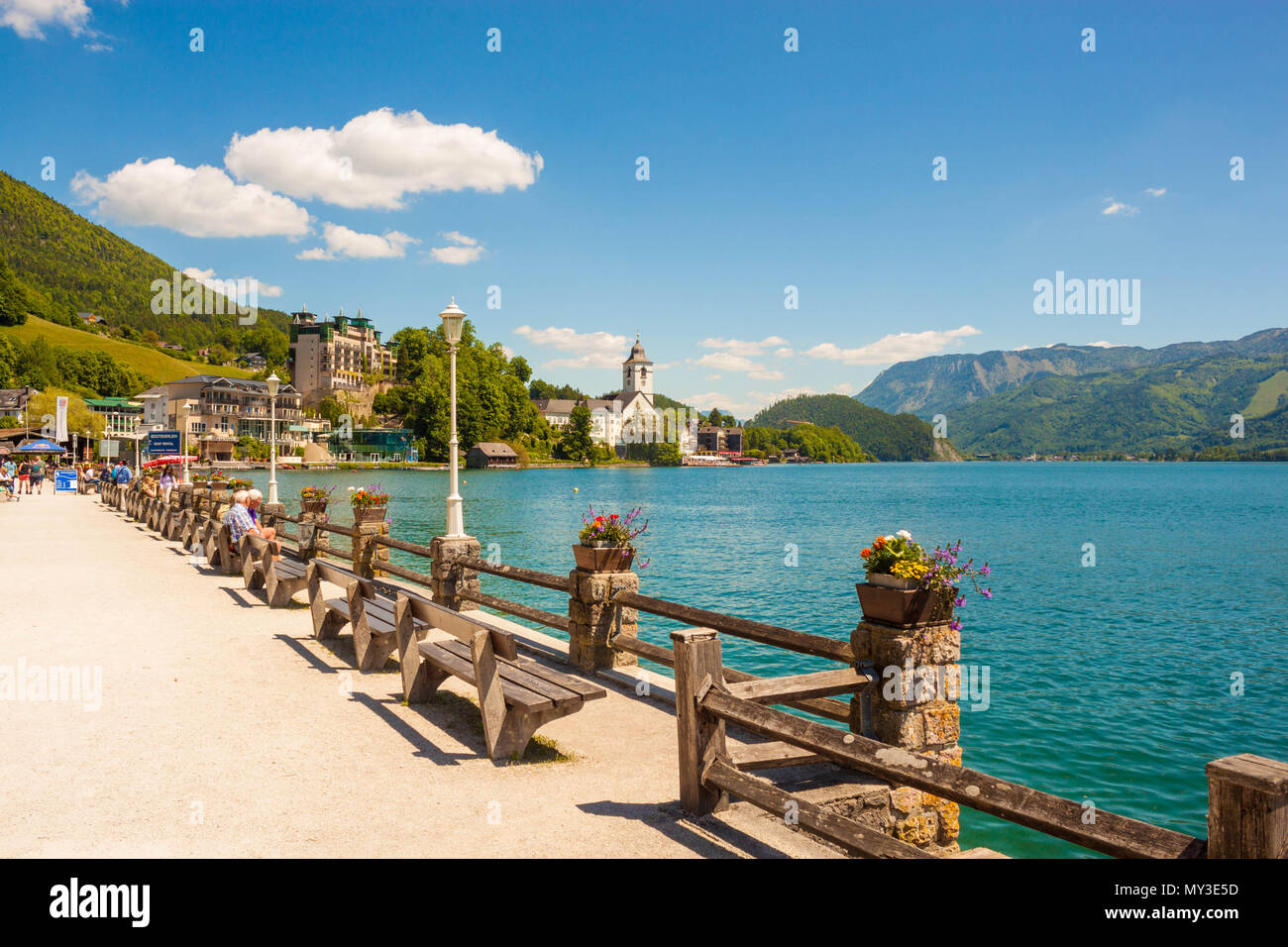St. Wolfgang, Austria - May 27, 2017: Waterfront promenade on alpine lake Wolfgangsee with a row of wooden benches. View of St.Wolfgang church  and mo Stock Photo