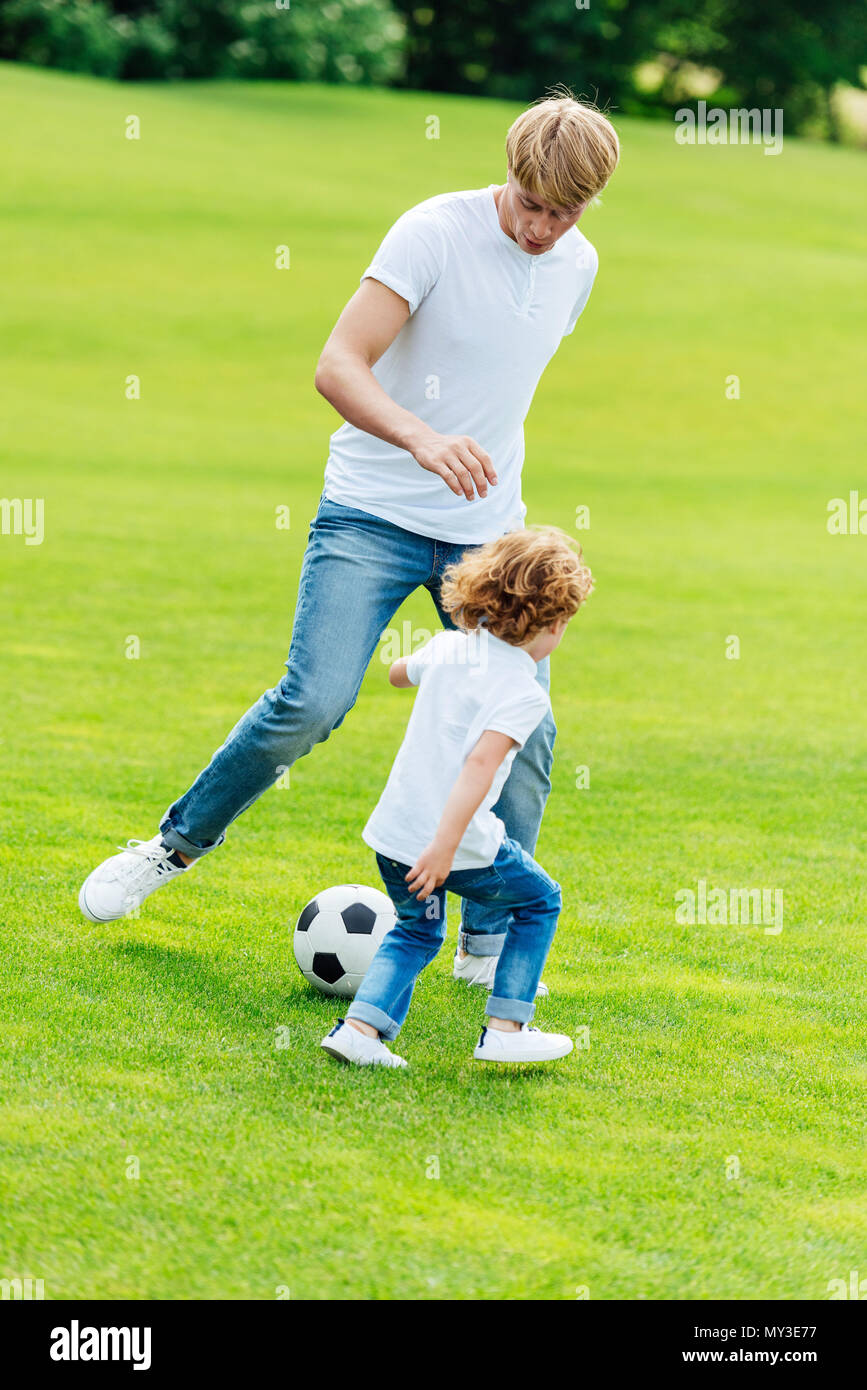 happy father and son playing soccer on green grass in park Stock Photo ...