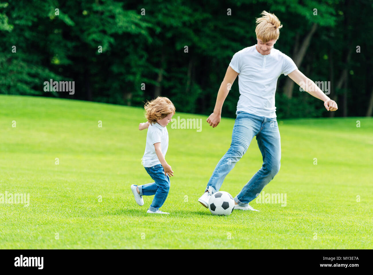 happy father and son playing soccer on green grass in park Stock Photo ...