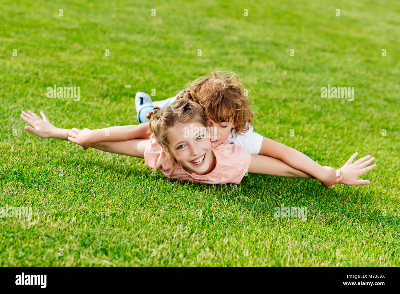 adorable brother and sister with arms outstretched lying on green grass