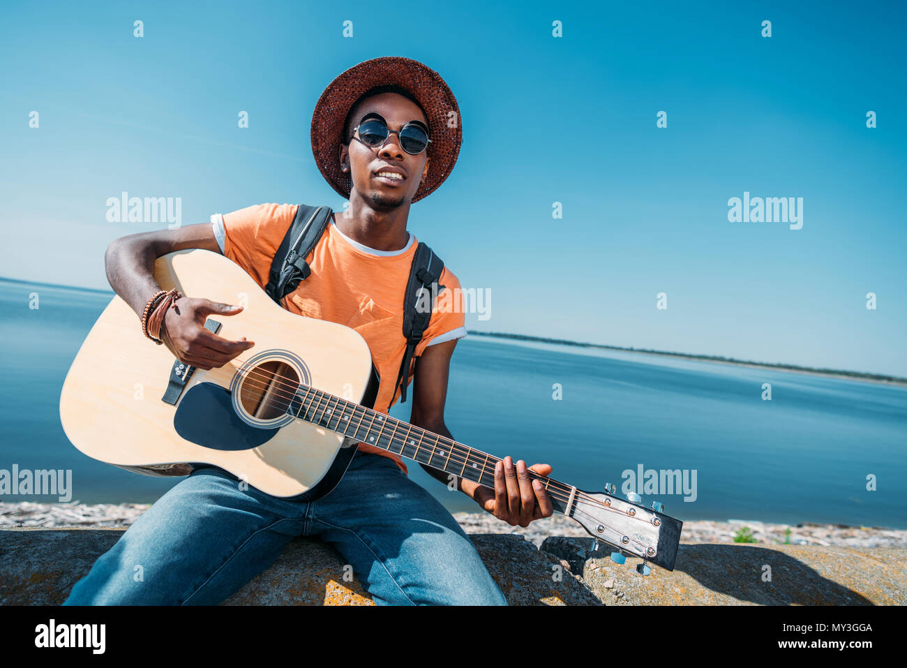 portrait of young african american man sitting on parapet and playing ...