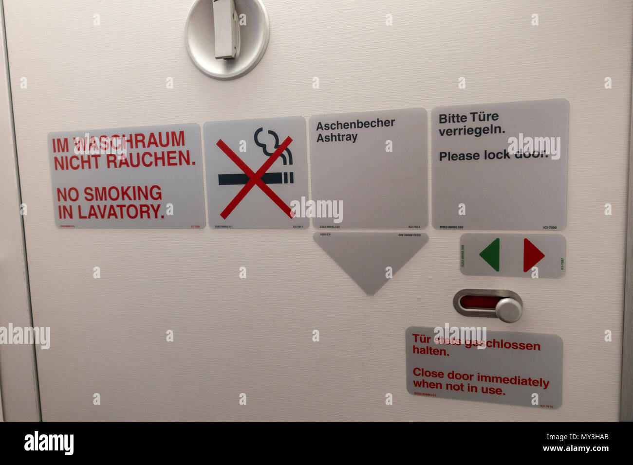 Airplane toilet door with No Smoking warning signs beside an ashtray sign on a European airline. Stock Photo