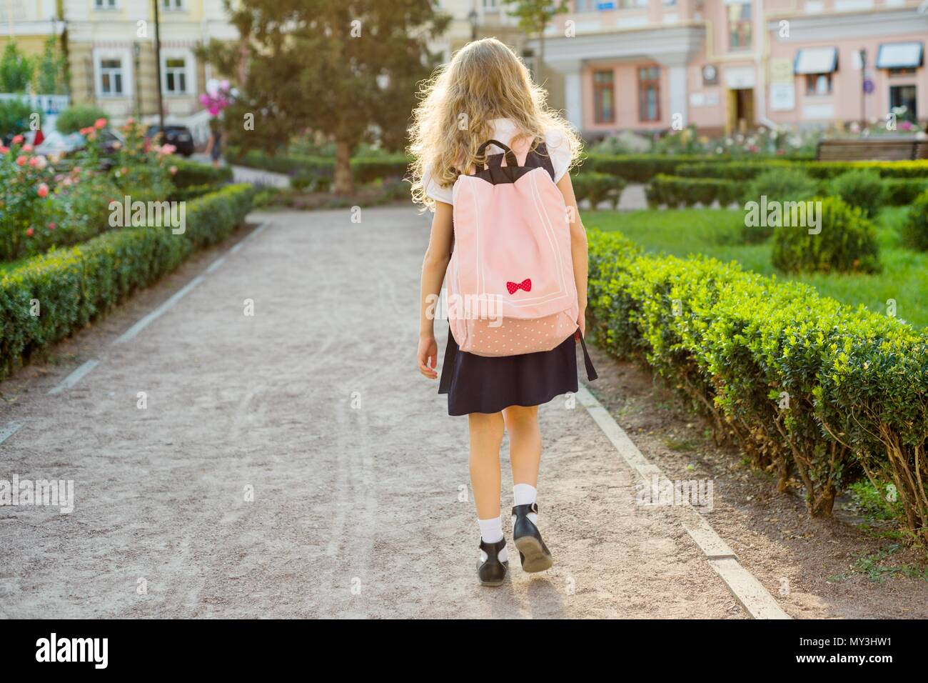 Rear view of young schoolgirl in uniform with backpack going to school ...