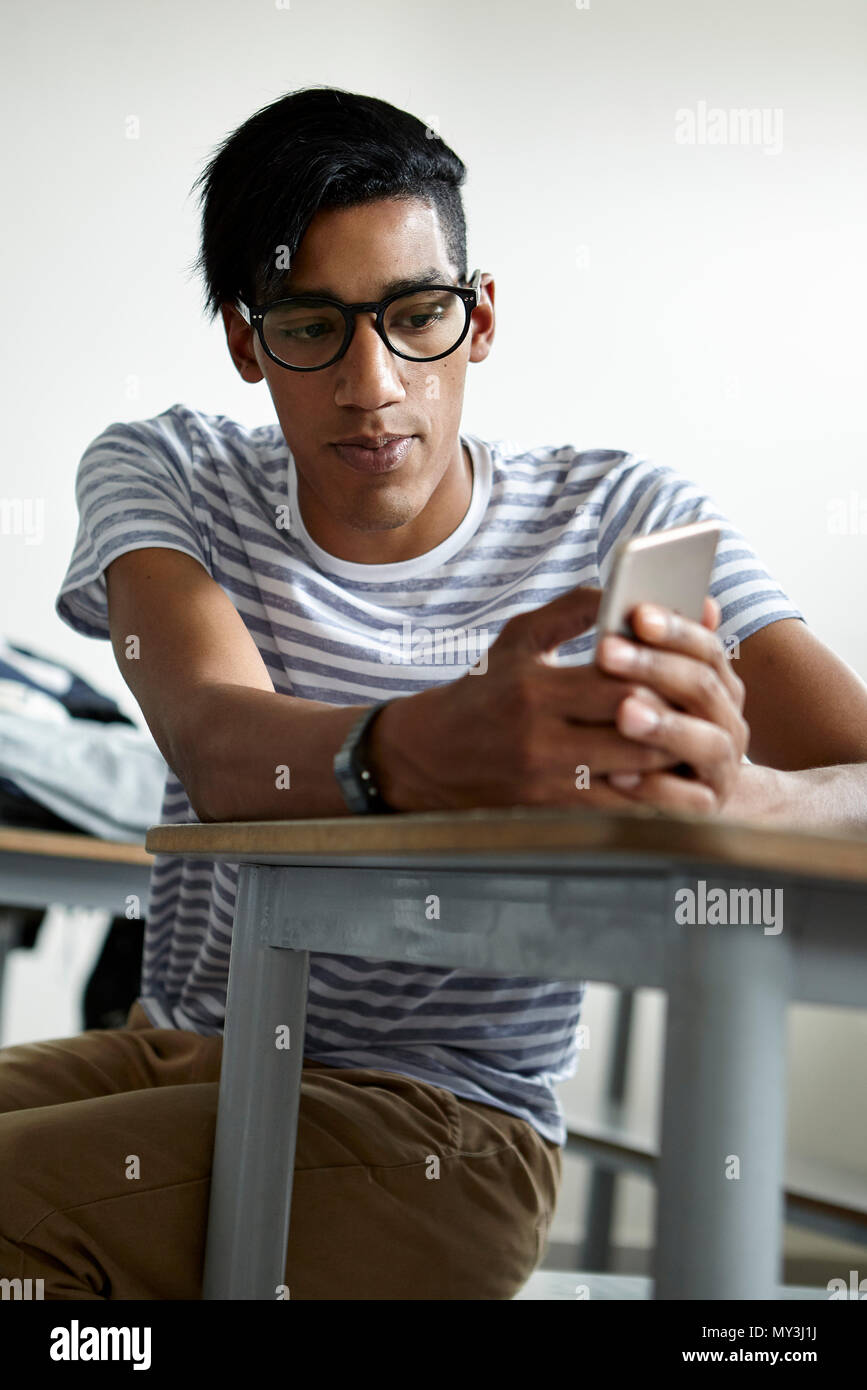 Student sitting at desk using smart phone Stock Photo