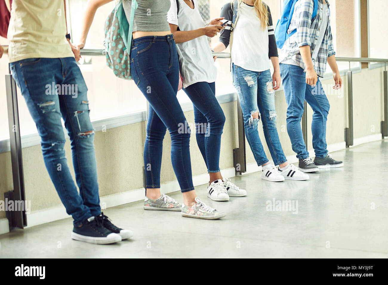 Casually dressed students leaning against railing in school corridor between classes Stock Photo