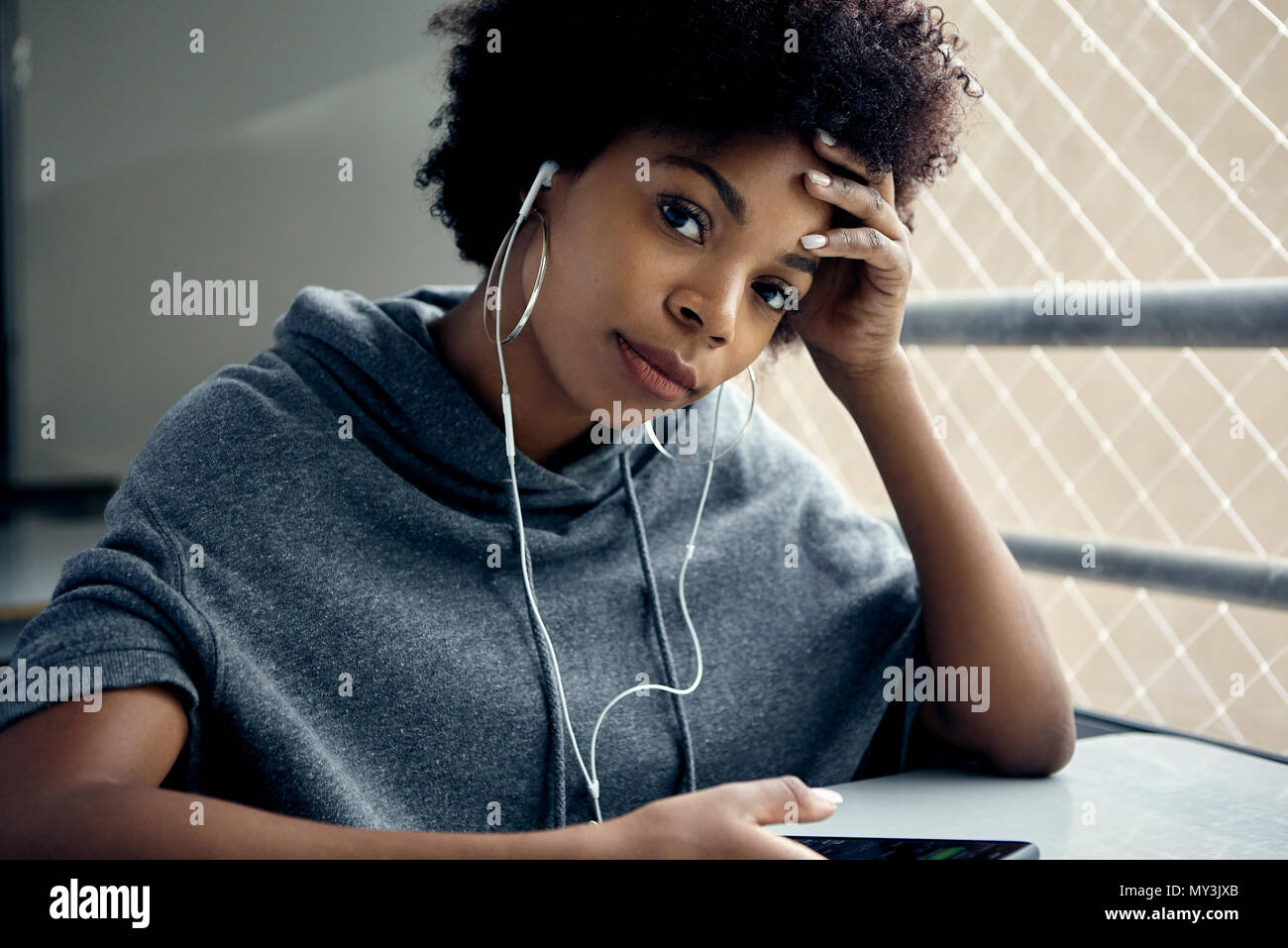 Young woman listening to earphones, holding head, portrait Stock Photo