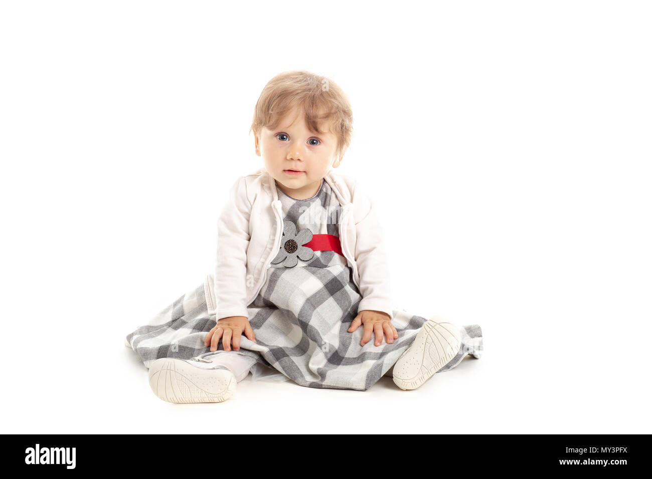 Elegant Happy baby girl 1 year old sitting on the studio floor. White Background. Concept Happiness. Stock Photo