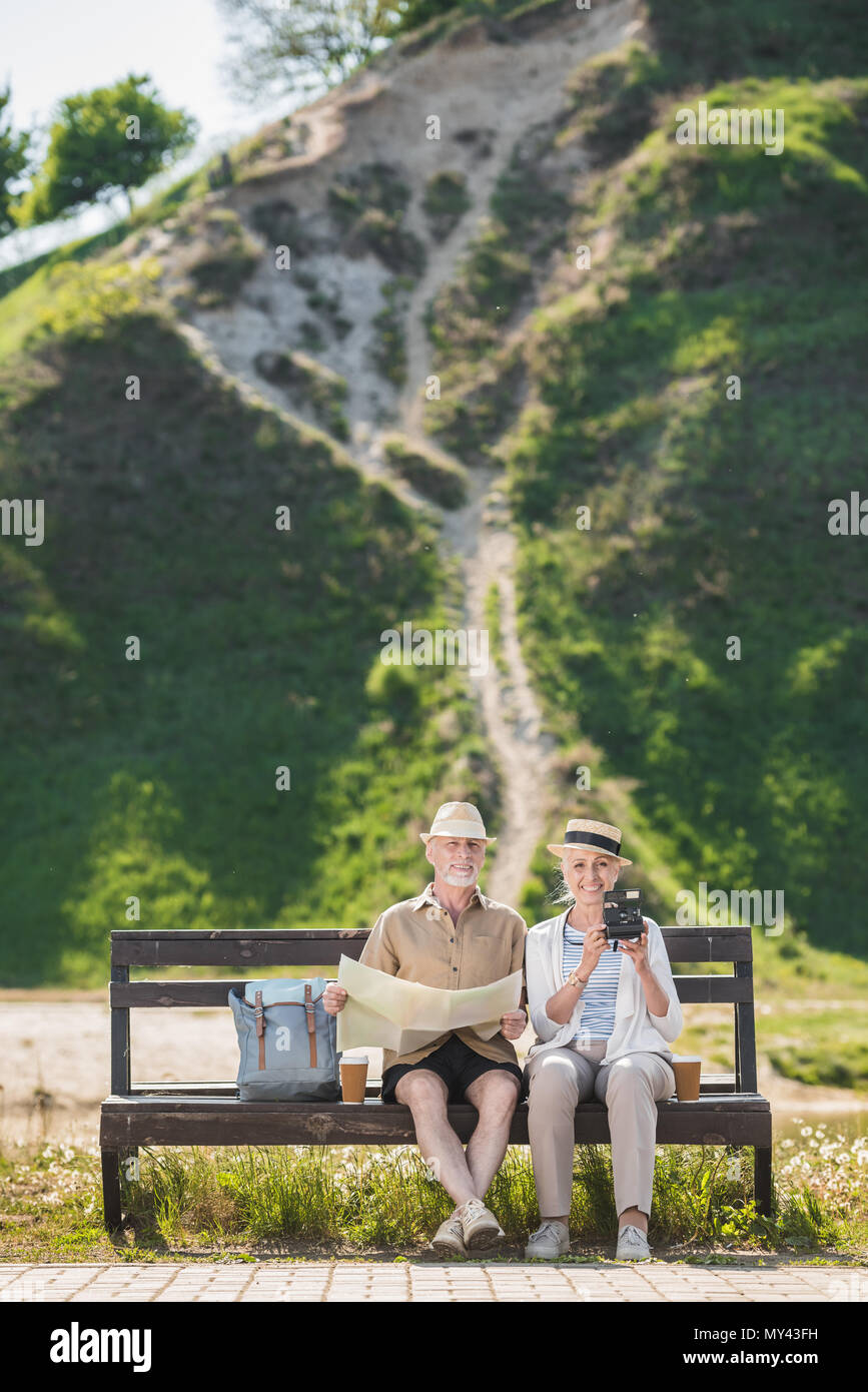 Happy senior couple of travelers sitting together on bench and holding ...