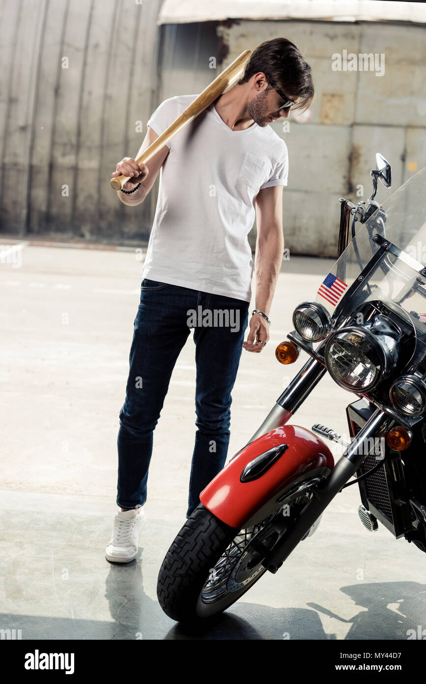 Handsome young man in sunglasses holding baseball bat on shoulder and