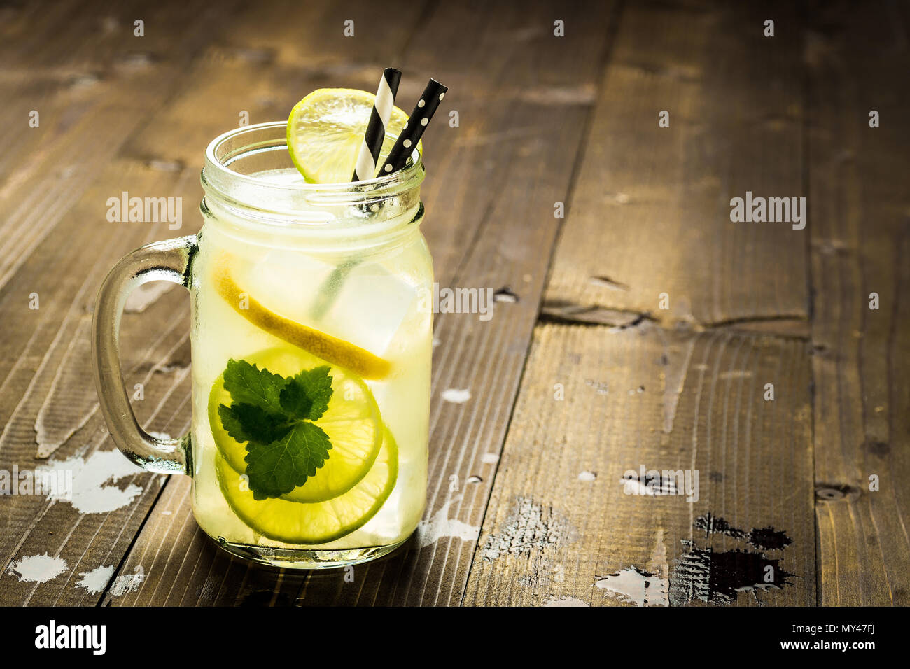 Cold Fresh Lemonade Mojito Cocktail with Ice, Lemon and Mint Leaves in Mason Jar on Rustic Dark Wooden Background. Summer Concept. Stock Photo