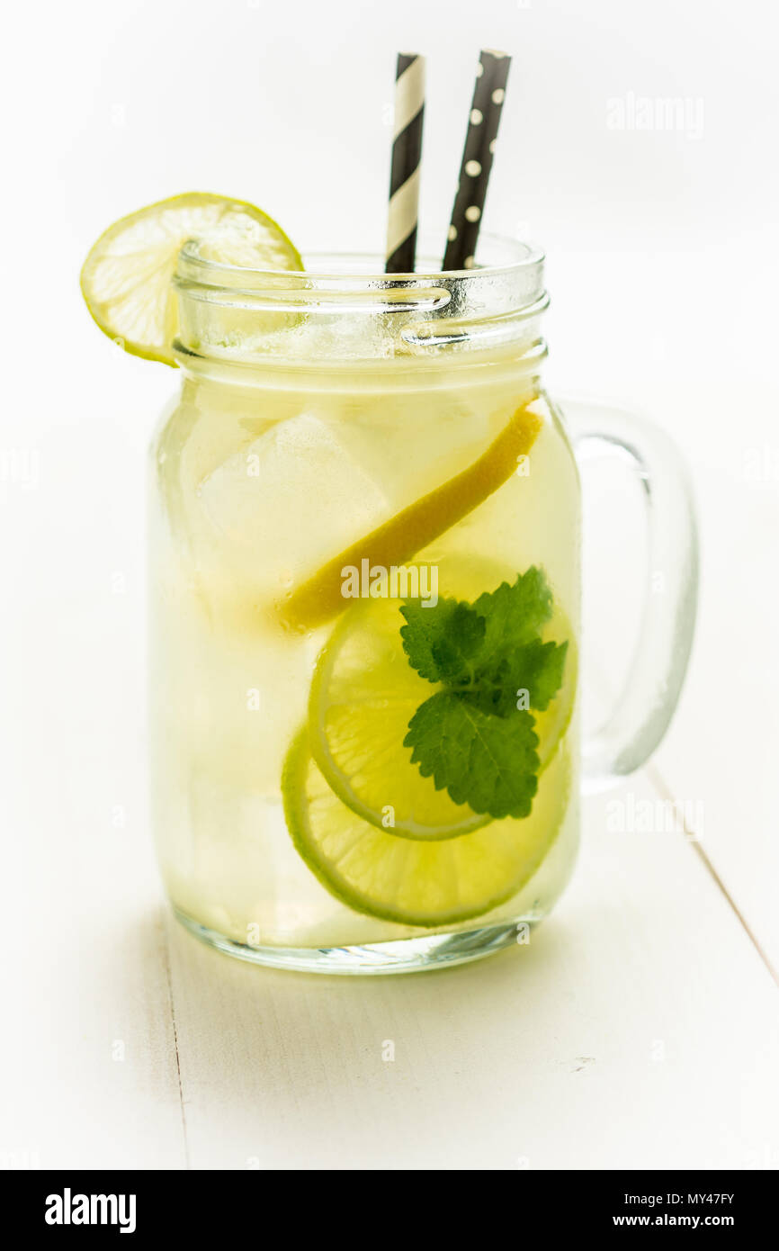 Lemonade Mojito Cocktail with Cold Fresh Ice, Lemon and Mint Leaves in Mason Jar on White Wooden Background. Bright Summer Concept. Stock Photo