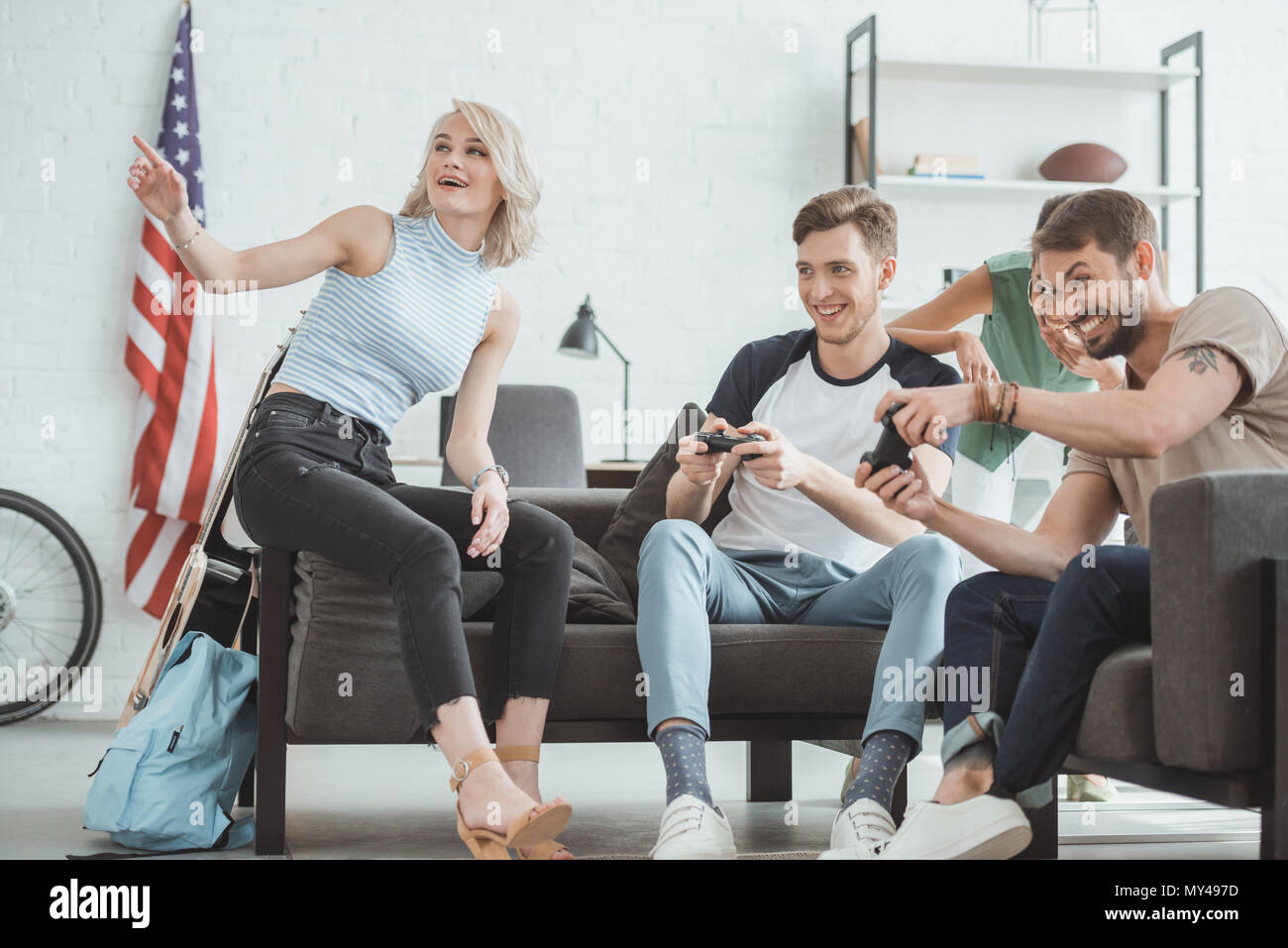 young men with joysticks playing video game and two smiling women sitting near Stock Photo