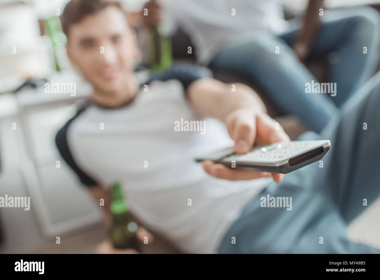 closeup shot of remote in hand of man sitting with bottle of beer Stock Photo