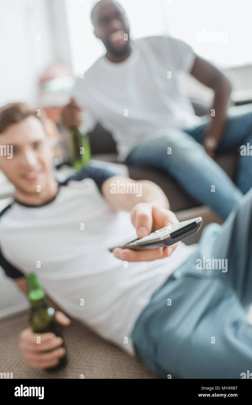 closeup shot of remote in hand of man sitting with bottle of beer near friend Stock Photo