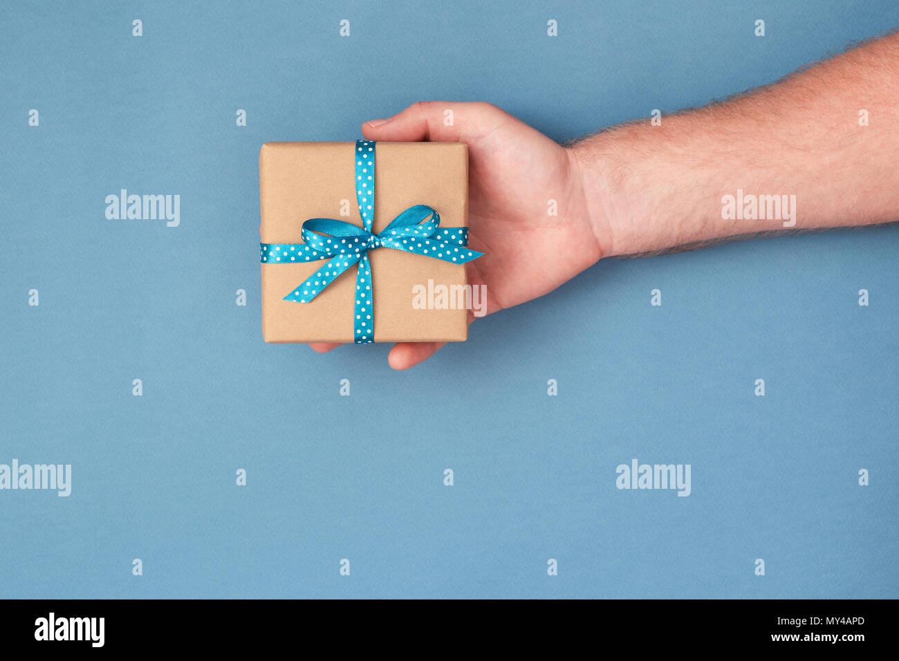 Man's hand holding kraft gift box tied with ribbon. Top view, holiday concept. Stock Photo