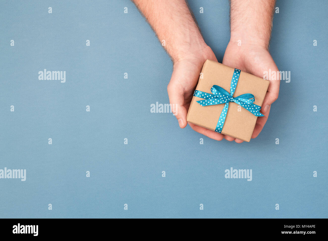 Man's hands holding kraft gift box tied with ribbon. Top view, holiday concept. Stock Photo