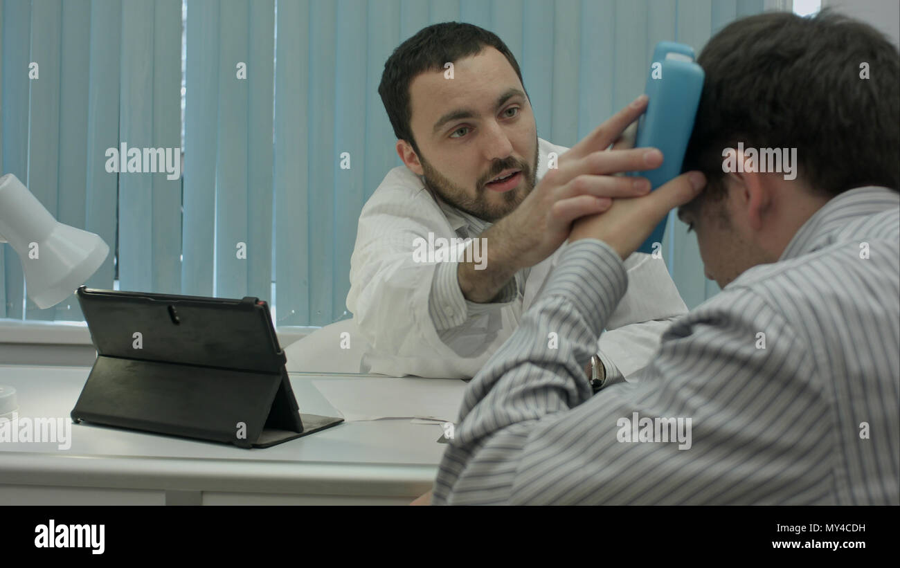 Male bearded doctor in clinic consult sick client with head injury ...