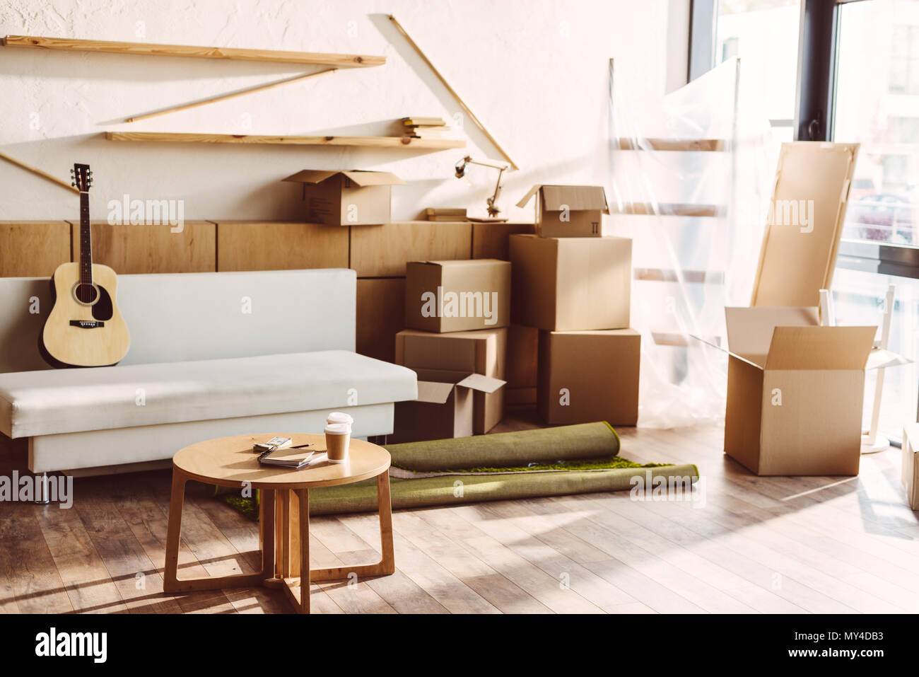 cardboard boxes, guitar on sofa and table with paper coffee cups in new ...
