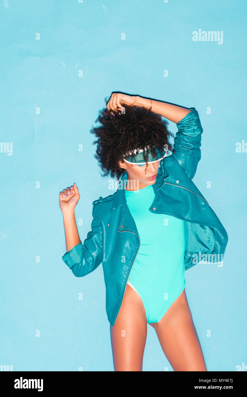 attractive afro model posing in turquoise bodysuit and blue leather jacket,  isolated on turquoise Stock Photo