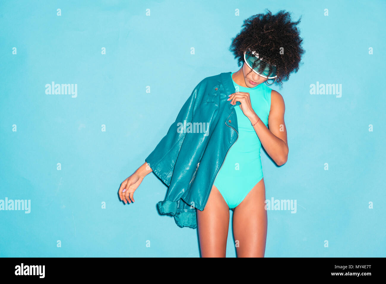 attractive stylish african american model posing in turquoise bodysuit and blue leather jacket,  isolated on turquoise Stock Photo