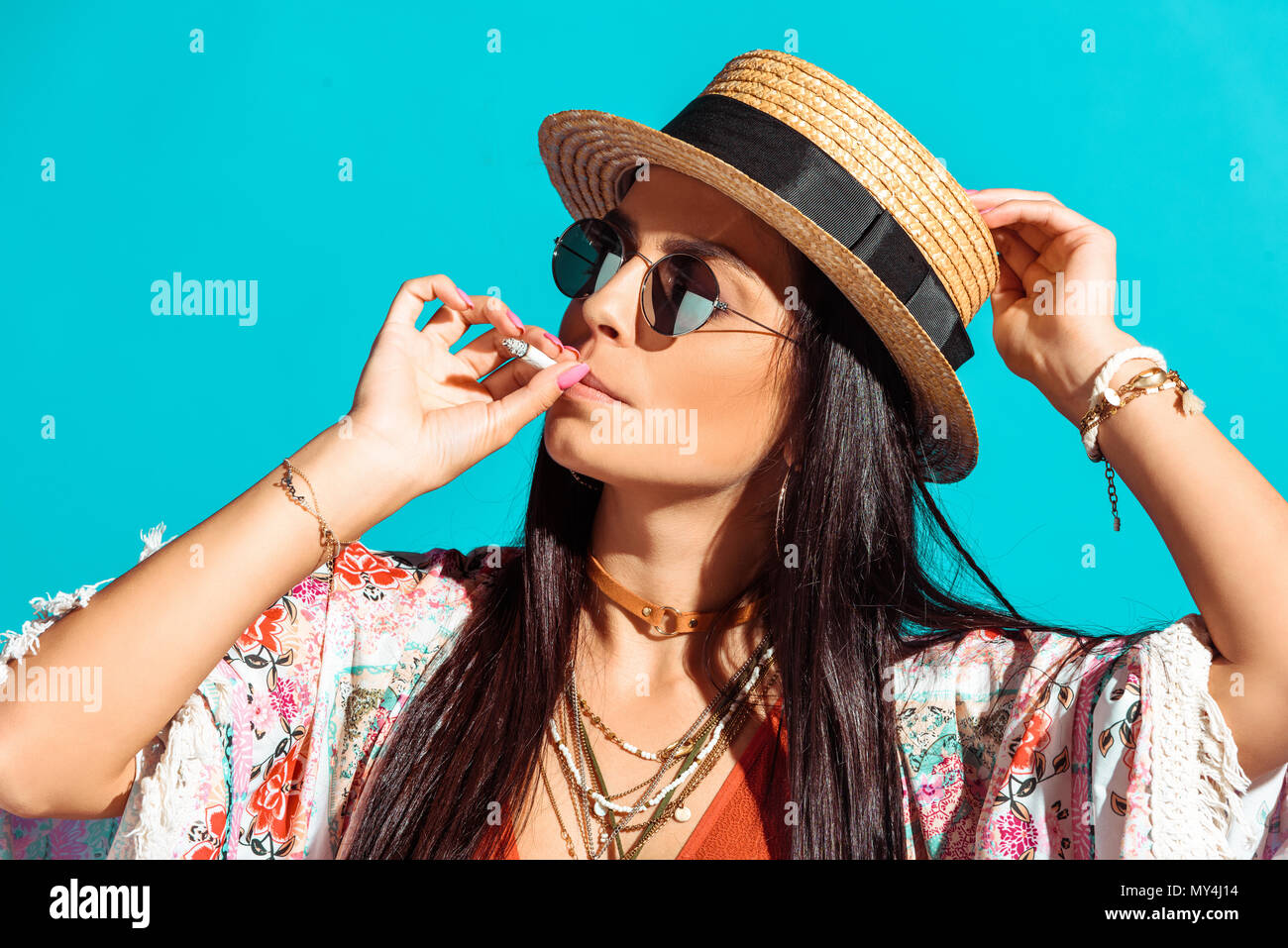 Attractive bohemian girl smoking cigarette isolated on turquoise Stock Photo