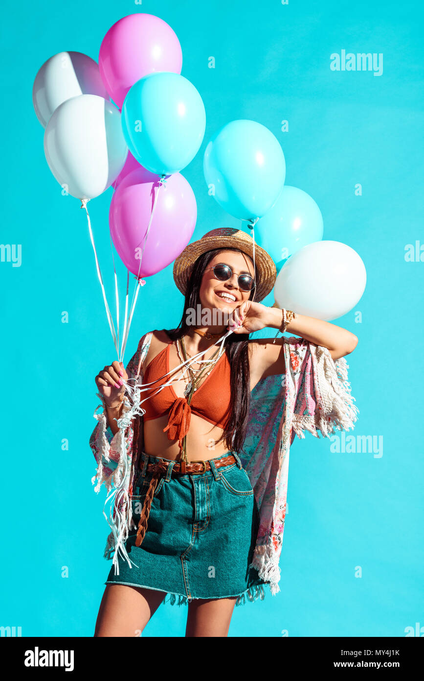 Smiling Hippie woman in sunglasses holding colored balloons isolated on turquoise Stock Photo