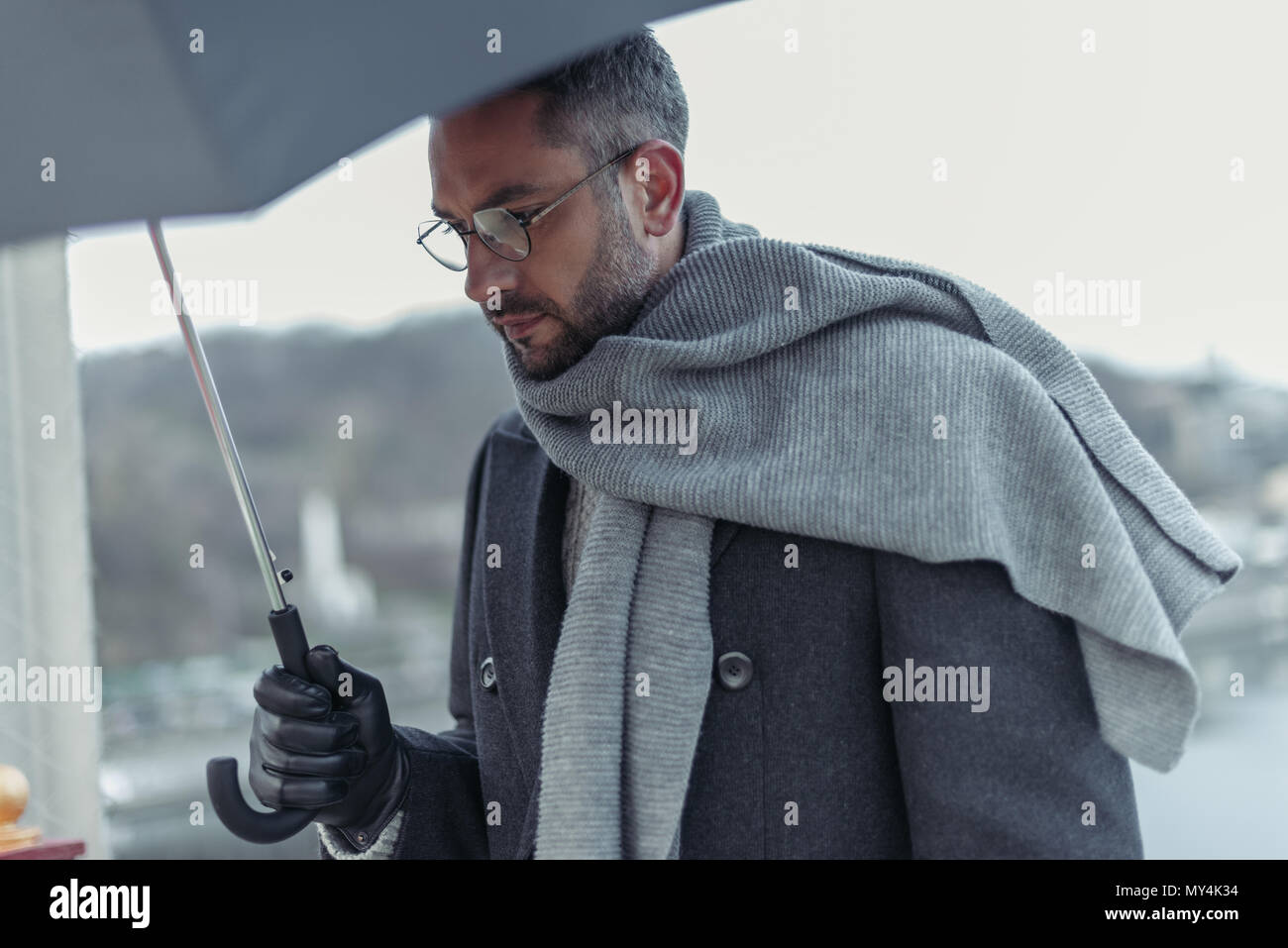 lonely sad man in scarf with umbrella walking under rain Stock Photo