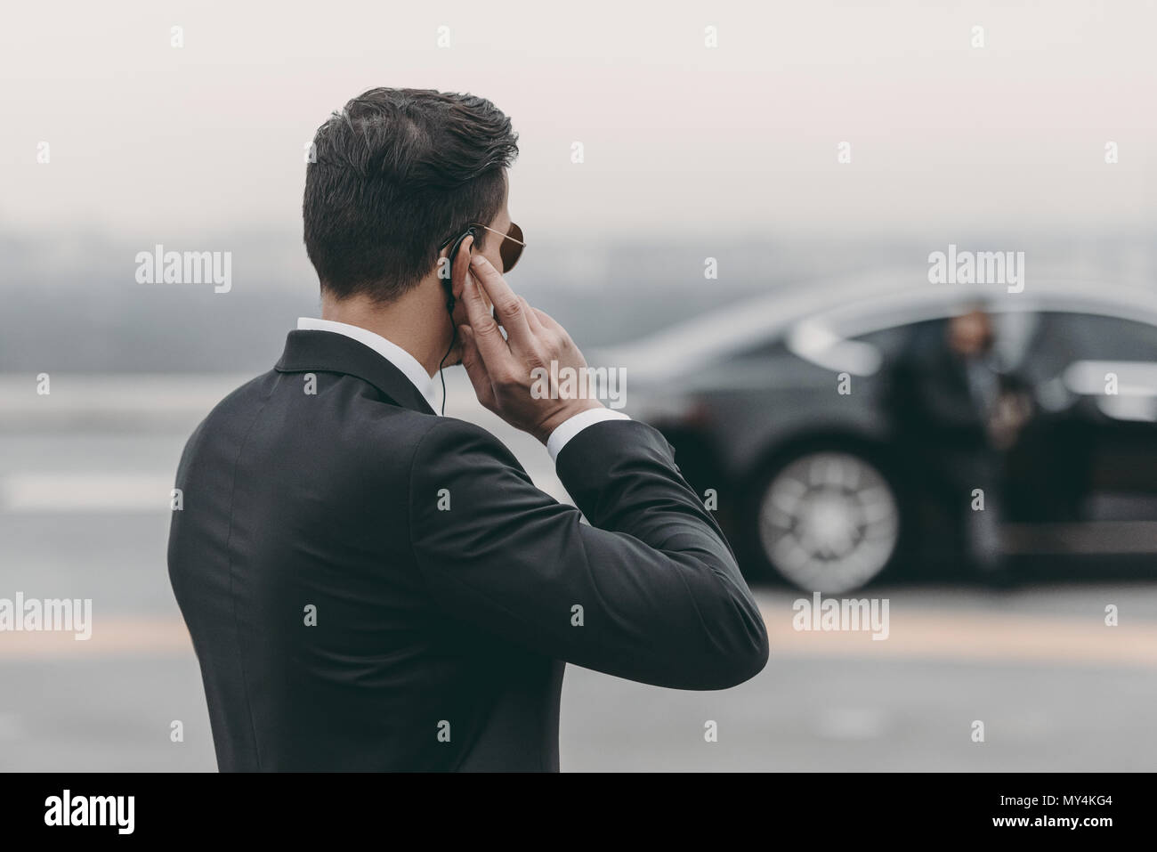 handsome bodyguard standing and listening message with security earpiece on helipad Stock Photo