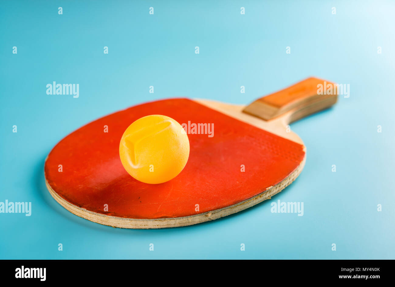 old pingpong racket and a dented ball on a blue background Stock Photo