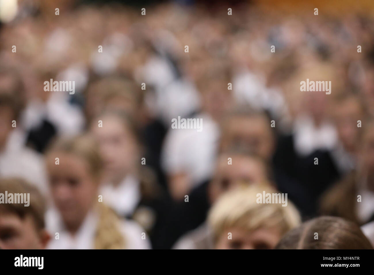 students in uniform sitting listening attentively at high school assembly facing the same direction. heavy blurred for anonymity and background effect Stock Photo