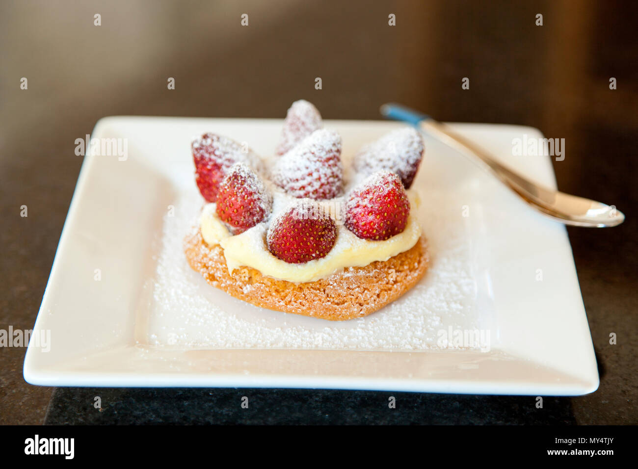 strawberry shortcake with cream and icing sugar on a white plate with a ...