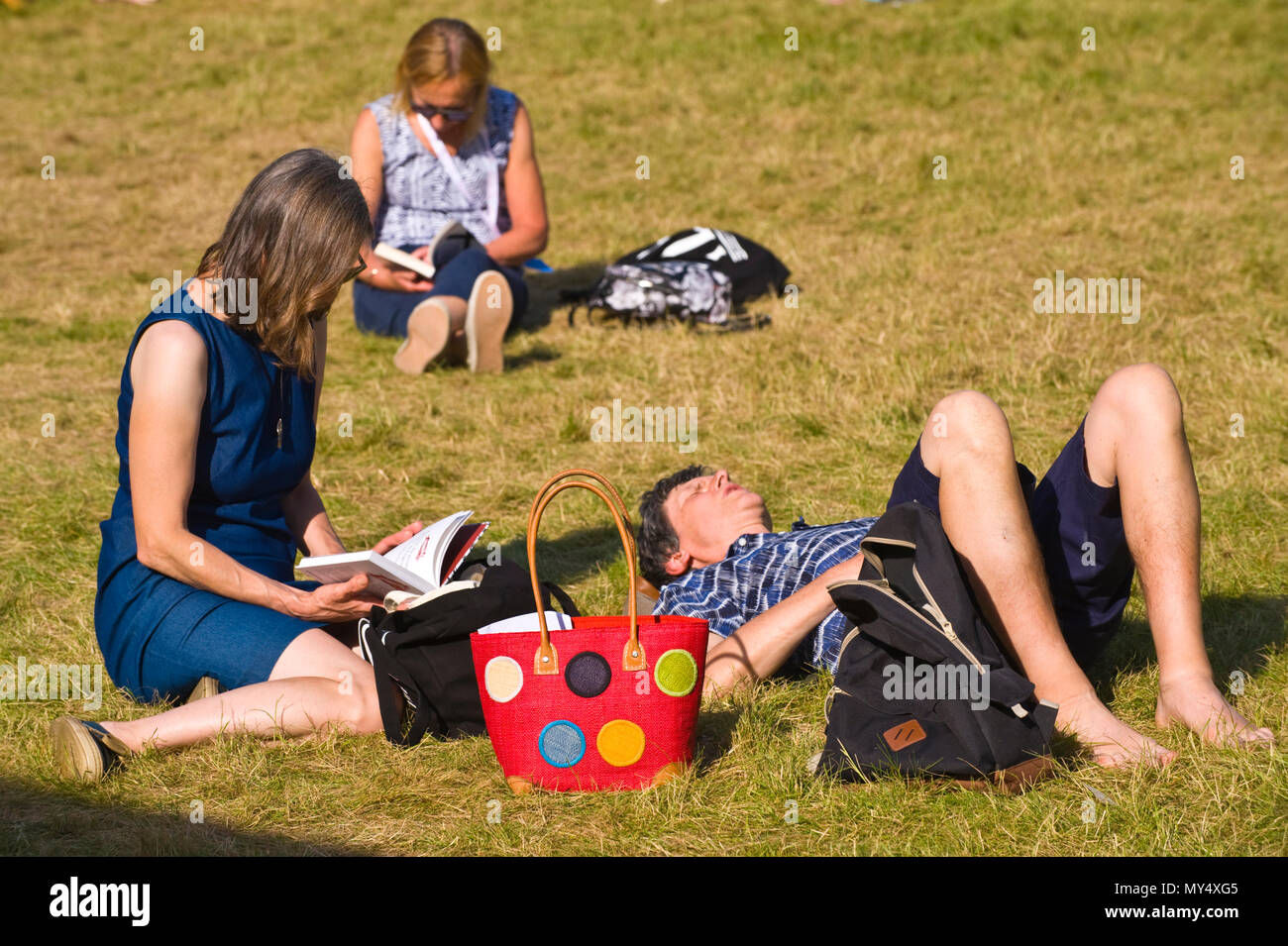 Women reading a books sitting on lawn in summer sunshine in garden area at Hay Festival 2018 Hay-on-Wye Powys Wales UK Stock Photo