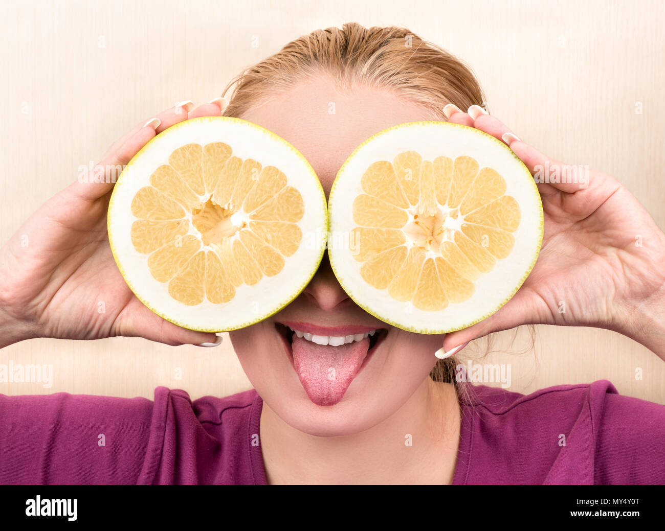 Beautiful girl showing tongue and holds the two halves of fruit Oroblanco in front Stock Photo