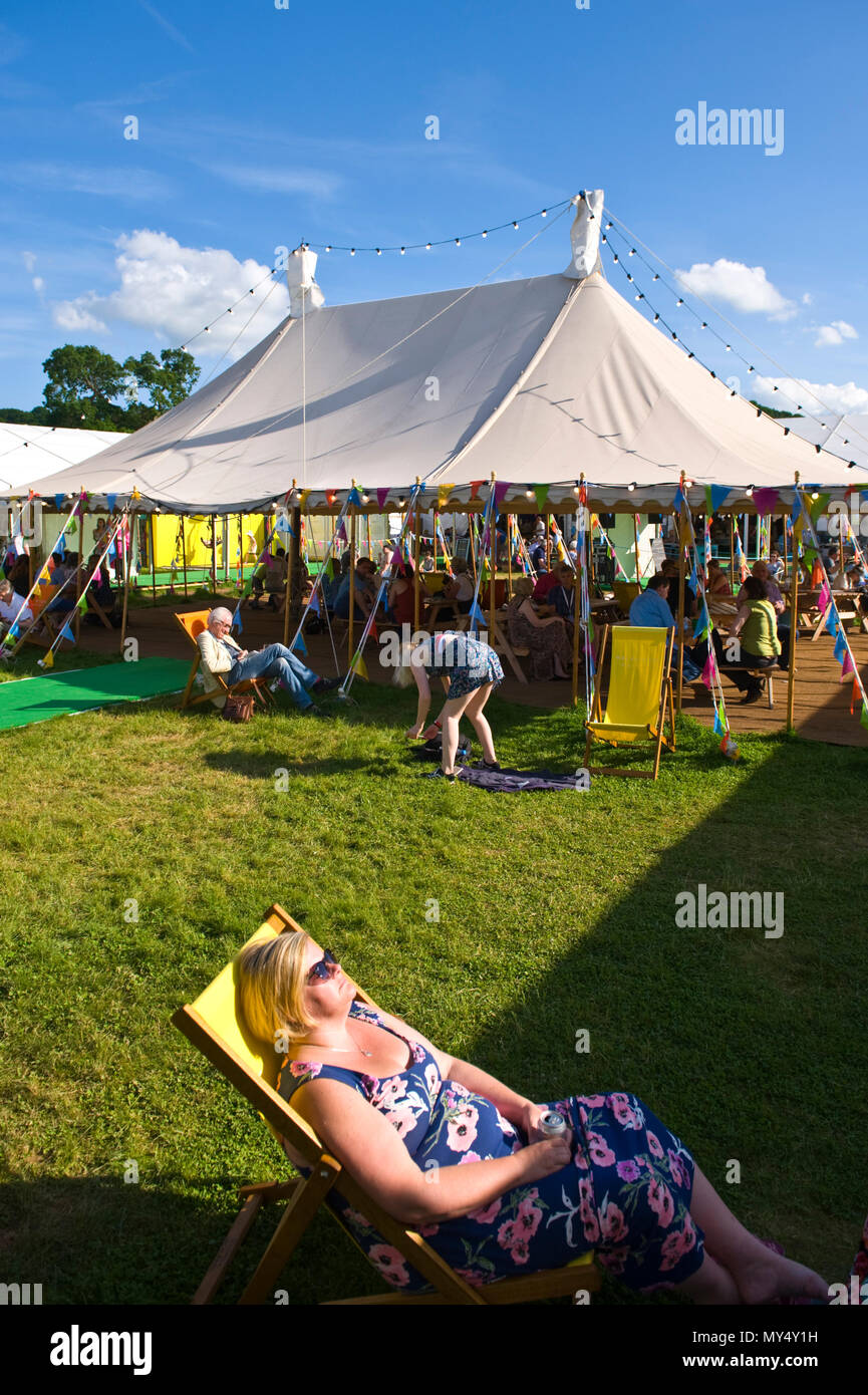 femaleWoman sitting in deckchair relaxing in late afternoon summer sunshine on lawn in garden area at Hay Festival 2018 Hay-on-Wye Powys Wales UK Stock Photo
