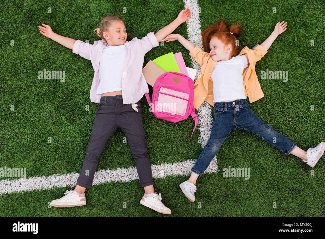 top view of beautiful happy schoolgirls smiling each other while lying ...