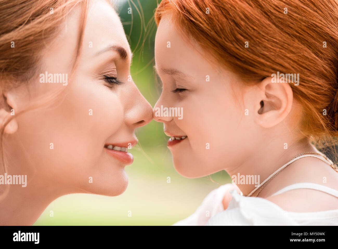 side view portrait of beautiful happy red haired mother and daughter touching noses at park Stock Photo