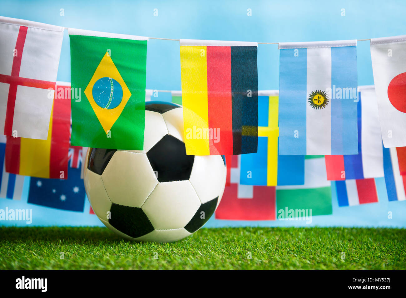 International world flag bunting hanging in celebration around a football sitting on grass Stock Photo