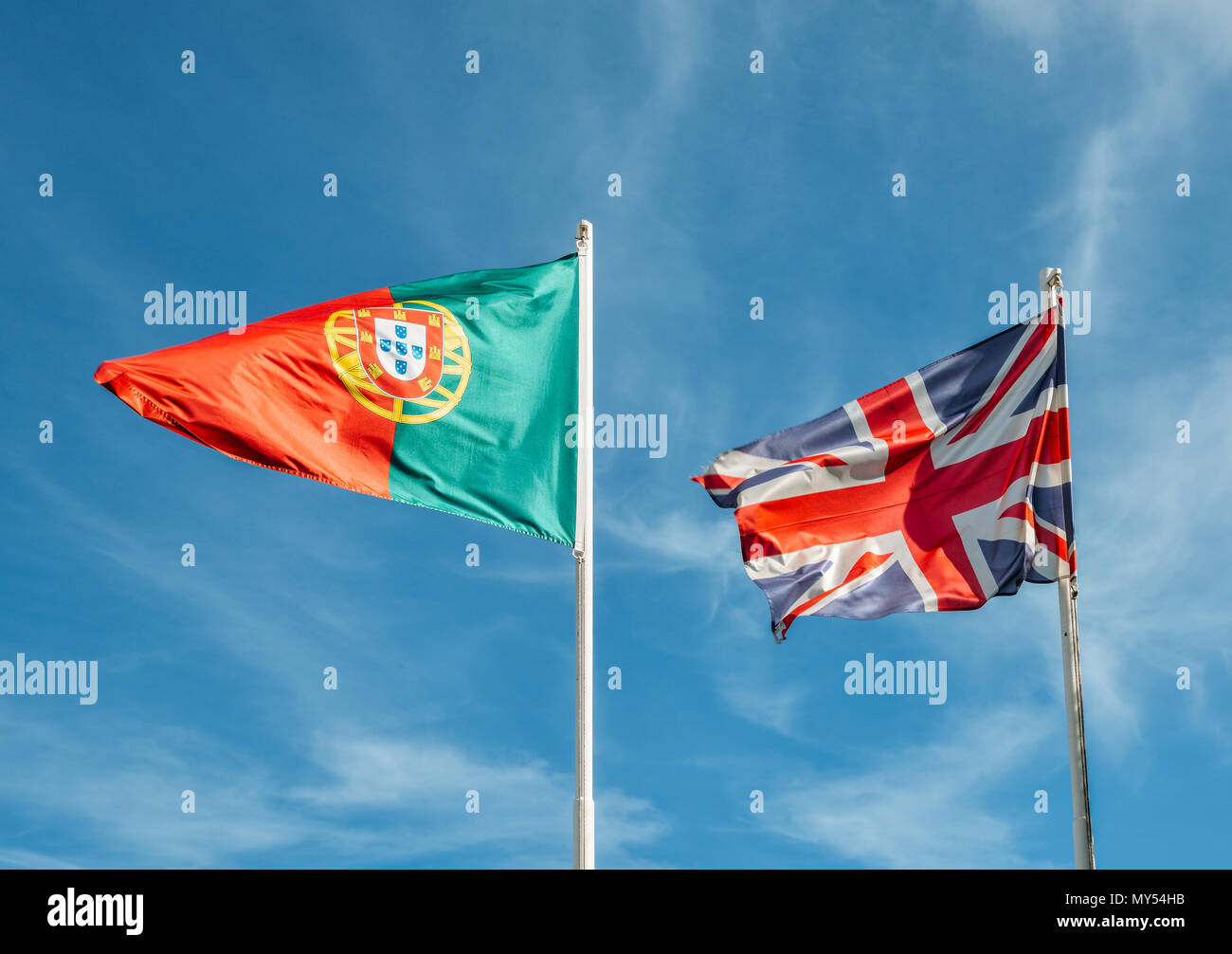 England and Portugal flag together on a mast against a blue sky Stock Photo