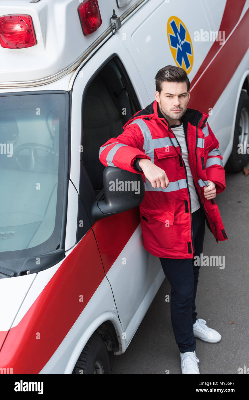 serious young male paramedic standing and leaning on ambulance Stock