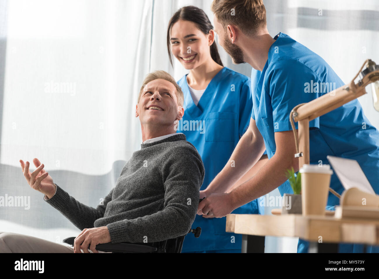 smiling doctors and patient on wheelchair talking in the hospital Stock Photo