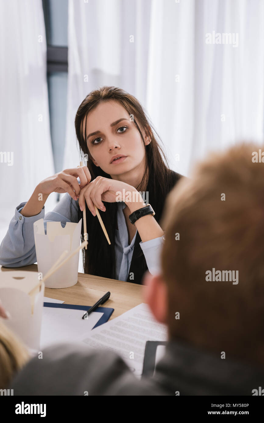 young overworked manageress sitting at workplace with box of chinese food and chopsticks Stock Photo