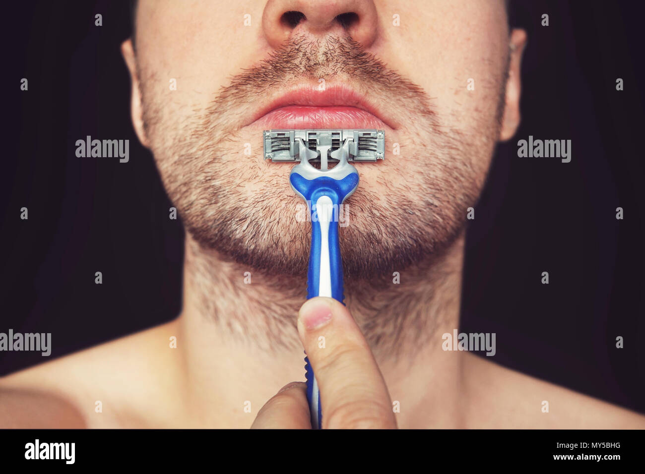 Young man without shaving cream on his face, grooming his beard with