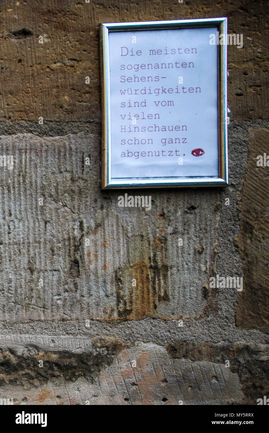 16 May 2018, Germany, Erfurt: A sign with the text 'Die meisten sogenannten Sehenswürdigkeiten sind vom vielen Hinschauen schon ganz abgenutzt' (lit. most of the so-called attractions have been worn down with lots of looking) hanging on a wall on the Kraemer bridge. The bridge is the longest in Europe with continuous occupied houses. It is one of Erfurt's landmarks. Hundreds of thousands of tourists coming to the city every year because of the bridge. Photo: Carsten Koall/dpa Stock Photo