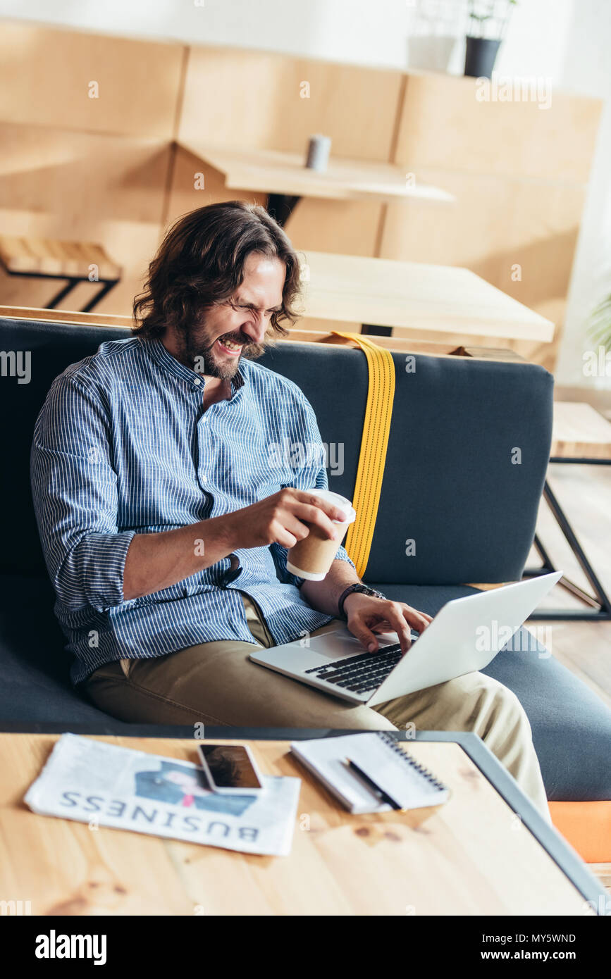 happy bearded man drinking coffee and using laptop Stock Photo