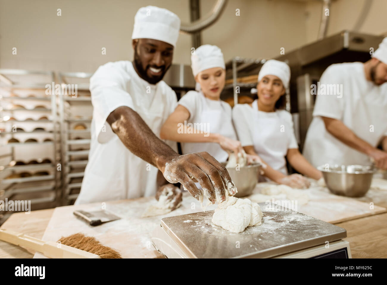 group of happy baking manufacture workers kneading dough together Stock