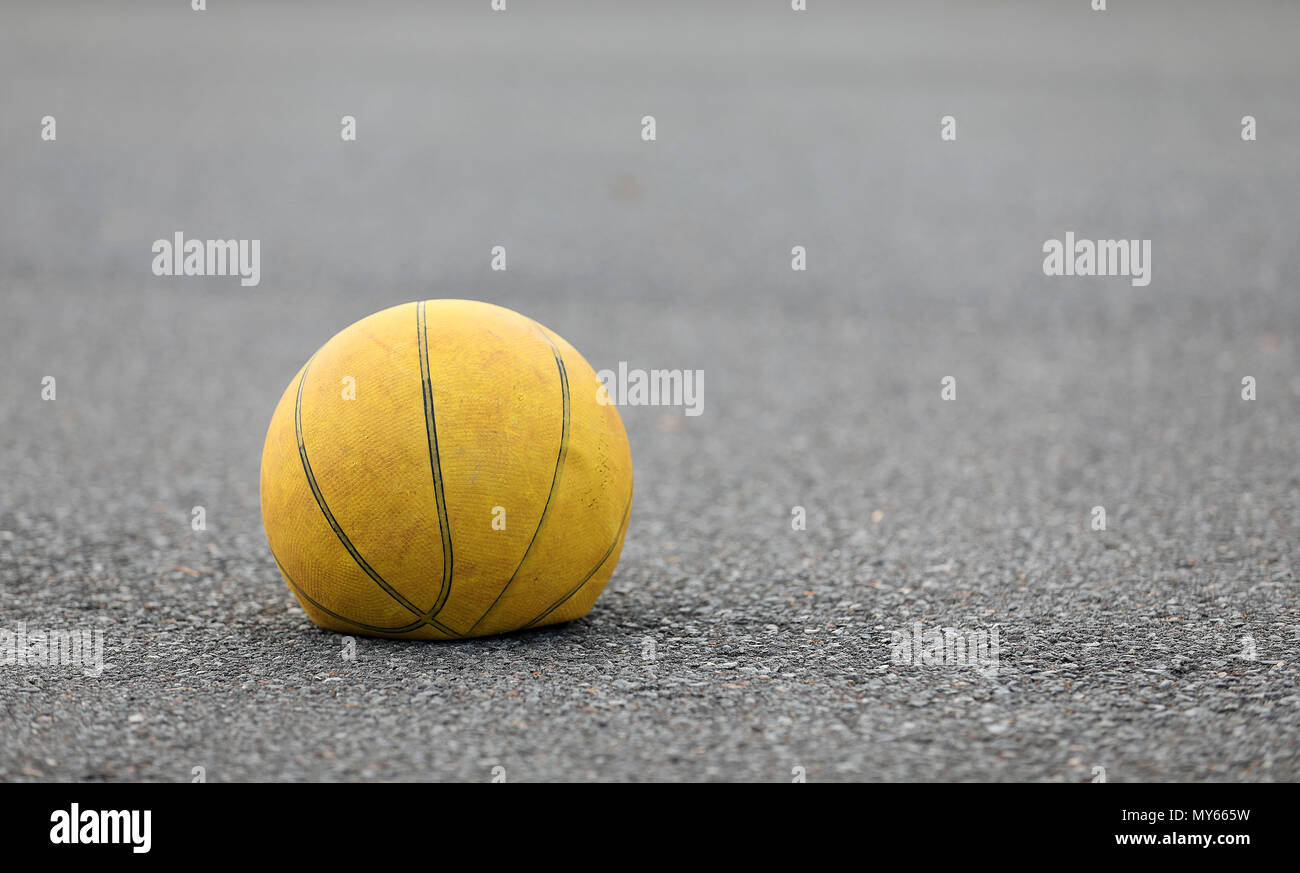 Left hand focus, old tired deflated let down yellow basketball on a road surafce concept. needs air, worn out spent and discarded sport equipment. Stock Photo