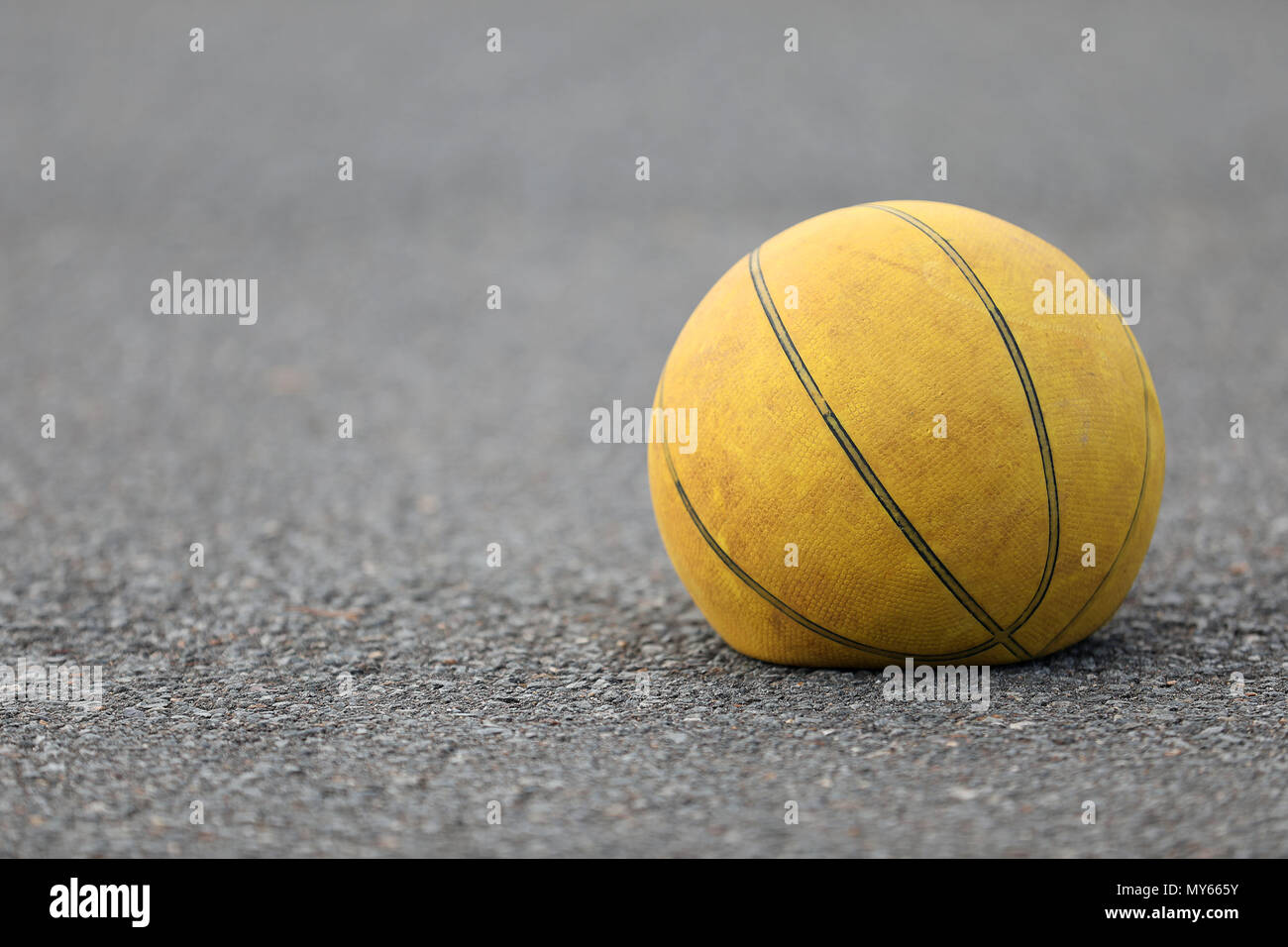Right hand focus, close up of old tired deflated let down yellow basketball on a road surafce concept. needs air, worn out spent and discarded sport e Stock Photo